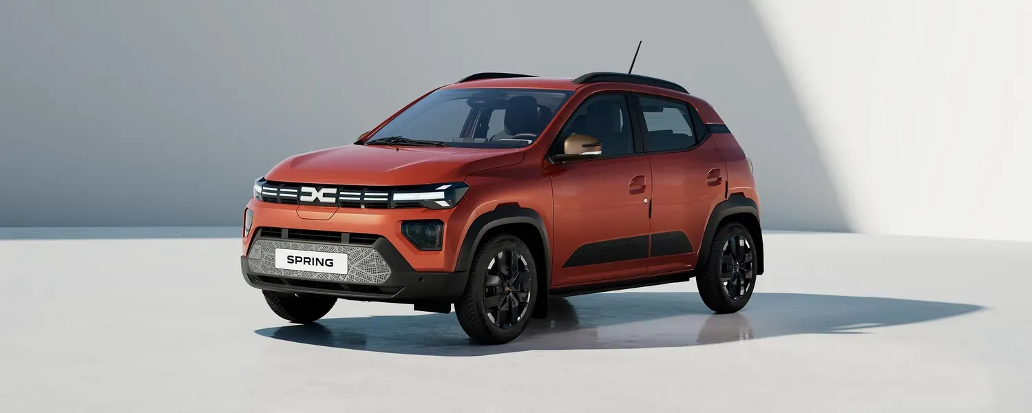 Dacia Spring in orange vor einer hellen Wand im Sonnenschein