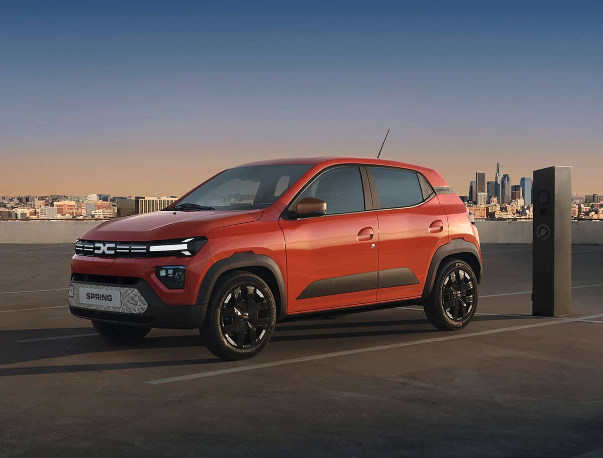 Der Dacia Spring an Ladesäule vor einer Stadtkulisse bei RRG.