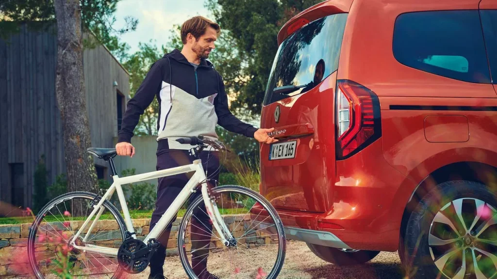 Mann mit einem Fahrrad öffnet den Kofferraum eines roten Renault Kangoo