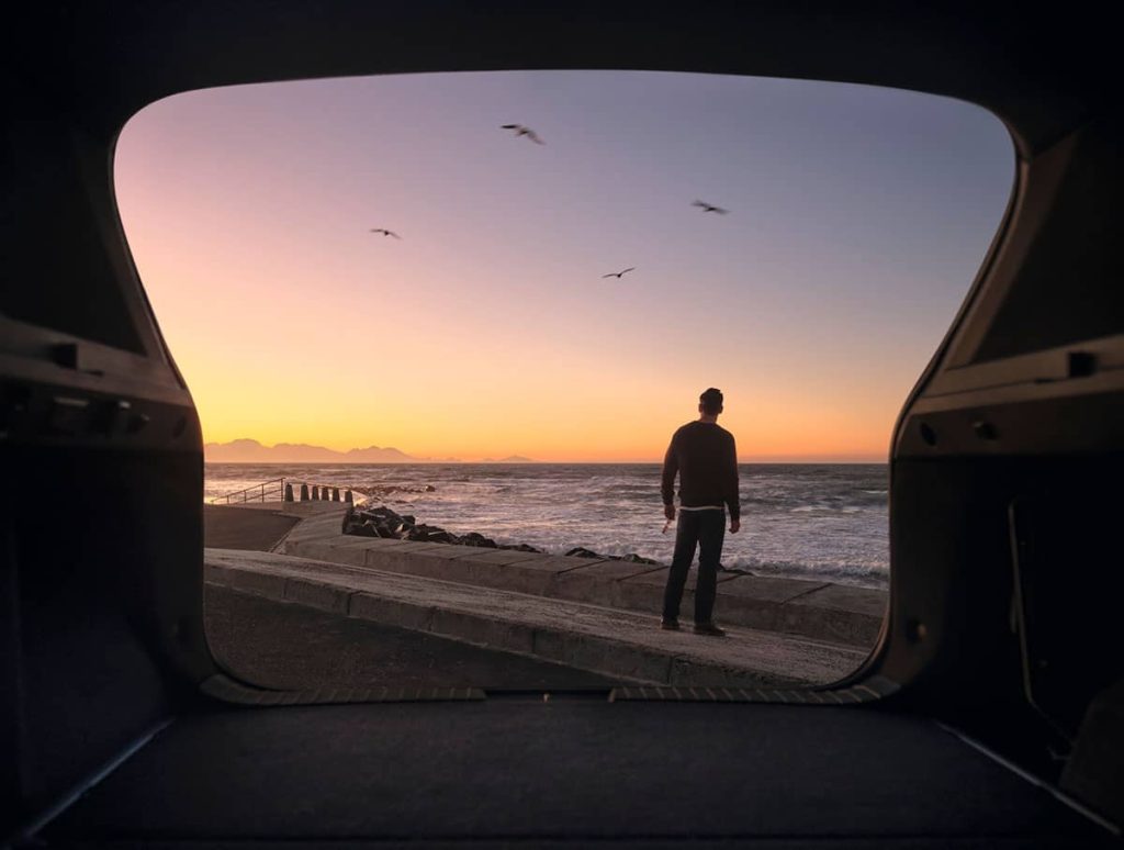 Blick aus dem Kofferraum eines Dacia auf eine untergehende Sonne am Strand