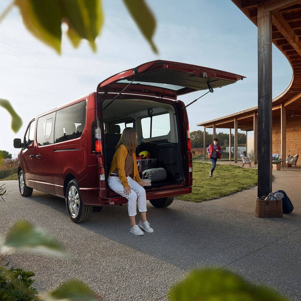 Renault Trafic Combi mit geöffnetem Kofferraum in der eine Frau sitzt die auf Ihr Kind wartet